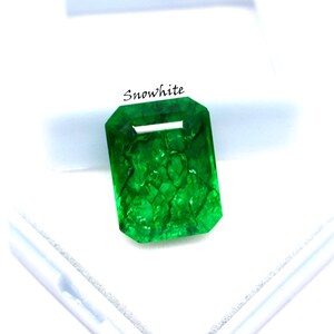 May include: A vibrant, emerald-cut green gemstone with the word "Snowwhite" printed on the top. The gemstone is a vivid green color and has internal inclusions. The gem is set against a white background.
