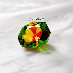 May include: A multi-faceted gem with a striking colour gradient, transitioning from green to yellow and red. The word "Snowwhite" is above the gem. The object is set against a white, marble-effect surface.