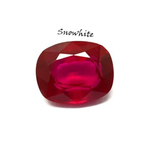 May include: A cushion-cut gemstone with a deep, vibrant red color and multiple facets that reflect light. The word Snowwhite is printed in black, stylized script above the gemstone, which features a polished, translucent surface.
