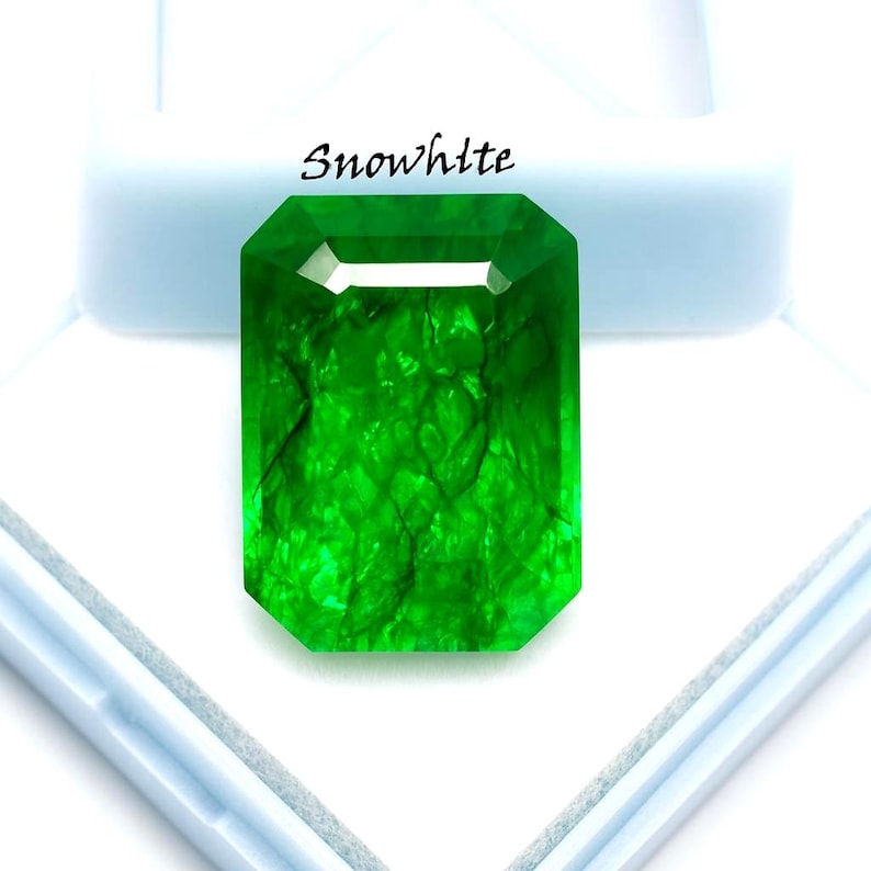 May include: A vibrant, emerald-cut green gemstone with internal veining. The gemstone is set against a white background and is labeled with the word "Snowhlte" in black text.