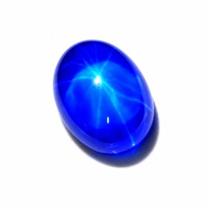 Puede incluir: Una piedra preciosa cabuj&oacute;n de color azul intenso y forma ovalada que presenta un efecto de estrella de seis rayos conocido como asterismo. La piedra tiene una superficie lisa, pulida y transl&uacute;cida que refleja la luz, creando un patr&oacute;n estelar brillante.