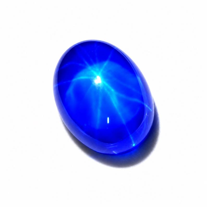 Puede incluir: Una piedra preciosa cabuj&oacute;n de color azul intenso y forma ovalada que presenta un efecto de estrella de seis rayos conocido como asterismo. La piedra tiene una superficie lisa, pulida y transl&uacute;cida que refleja la luz, creando un patr&oacute;n estelar brillante.