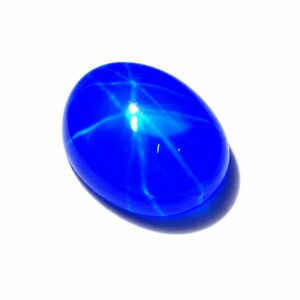 Puede incluir: Una piedra preciosa cabuj&oacute;n de forma ovalada en color azul vibrante que presenta un patr&oacute;n de estrella de seis puntas distintivo en su superficie pulida y abovedada. La piedra muestra un color azul profundo y saturado con un efecto.
