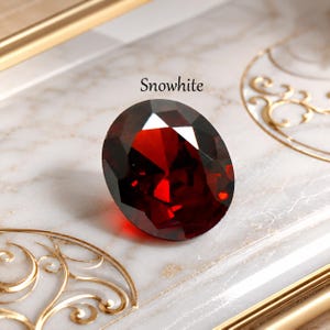 Può includere: Una gemma rosso scuro dal taglio ovale con molteplici sfaccettature che riflettono la luce. La pietra è posizionata vicino al testo "Snowwhite" stampato con un carattere scuro. La gemma presenta una ricca tonalità cremisi con bordi netti.