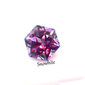 May include: A faceted hexagonal gemstone displaying deep purple and magenta hues with reflective surfaces. The stone features a brilliant cut that creates sharp geometric light patterns. The word Snowwhite is printed in black text below the gem.
