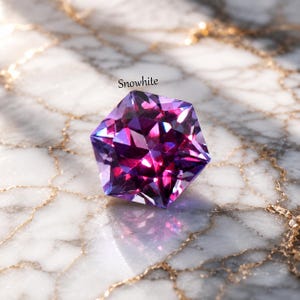 May include: A faceted, pentagonal gemstone displaying deep purple and magenta hues with reflective surfaces. The stone features the word Snowwhite printed in small black text above it, showcasing sharp geometric angles and brilliant light refraction.