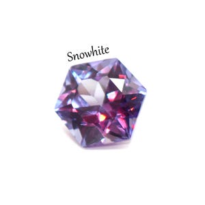 May include: A faceted hexagonal gemstone displaying a color-shifting gradient of deep purple, magenta, and blue tones. The stone features a brilliant cut with sharp geometric edges and reflective surfaces. The word Snowwhite is printed above the gem.