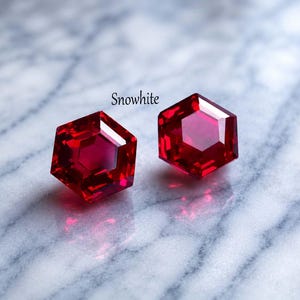 May include: Two hexagonal, red gemstones with the word "Snowwhite" above them. The gems are a deep red colour and reflect light, creating a sparkling effect. The background is a light grey and white marble.