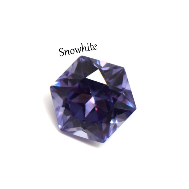 May include: A faceted, hexagonal-shaped gemstone in a deep purple hue with light-reflecting surfaces. The word Snowwhite is printed in black text above the stone. The gem displays sharp geometric edges and a brilliant, polished finish throughout.