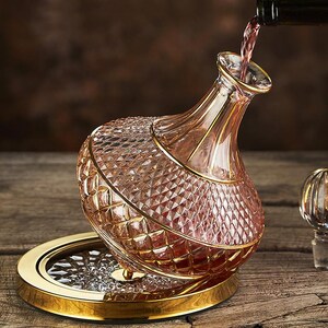 May include: A crystal wine decanter with a diamond-cut pattern and gold trim is being filled with red wine. The decanter sits on a gold-rimmed base. The wine is being poured from a dark bottle.