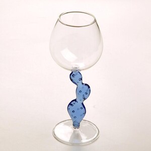 May include: A clear glass wine glass with a unique blue cactus-shaped stem. The stem has a series of bubbles. The glass has a round bowl and a flat base. The glass is designed for serving wine.