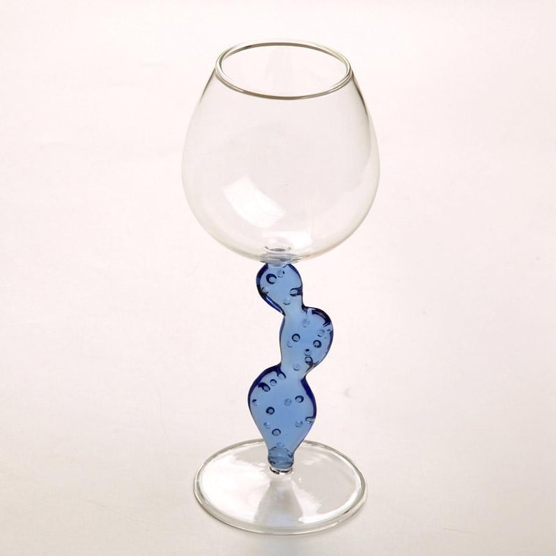 May include: A clear glass wine glass with a unique blue cactus-shaped stem. The stem has a series of bubbles. The glass has a round bowl and a flat base. The glass is designed for serving wine.