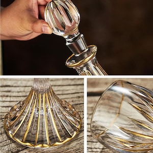 May include: A clear glass decanter with a gold rim and accents. The stopper is clear with a ribbed design. The base of the decanter has a fan-like pattern with gold detailing. The decanter is on a wooden surface.