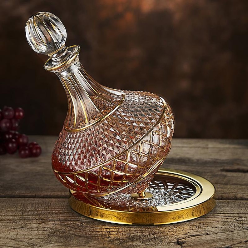 May include: A crystal glass decanter with a diamond pattern and gold trim, filled with red liquid. The decanter rests on a gold-rimmed tray with a decorative base. The stopper is a clear, round shape.