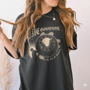 May include: Black t-shirt with the words "Wave Goodbye" above a circular graphic featuring a clock face and a silhouetted figure. The phrase "To The End Of Beginning" is below the graphic.