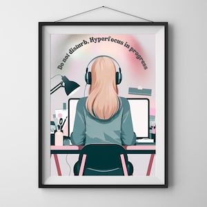 Puede incluir: Impresión artística enmarcada que muestra a una persona con cabello rubio usando auriculares, sentada en un escritorio con una computadora. El texto "Do not disturb, Hyperfocus in progress" está arqueado sobre la persona. También se ve una lámpara de escritorio y útiles de oficina.