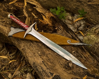 May include: A detailed fantasy dagger with a silver blade and ornate hilt, resting on a weathered log. The handle is red with white accents. The dagger is sheathed in a tan leather scabbard with silver detailing.