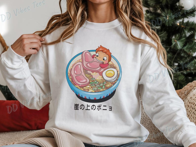 May include: White long-sleeve sweatshirt featuring a colorful illustration of a ramen bowl with a cartoon character. The bowl contains noodles, meat, an egg, and green onions. Japanese text is below the bowl.
