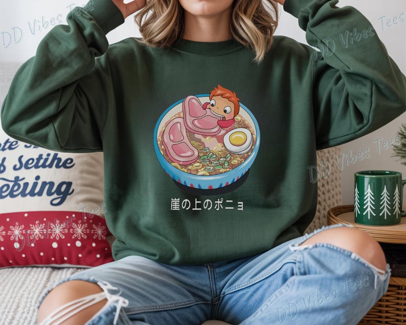 May include: Dark green sweatshirt featuring a colorful illustration of a bowl of ramen with a cartoon character. The ramen includes meat, an egg, and vegetables. Japanese text is below the bowl. The sweatshirt has long sleeves.