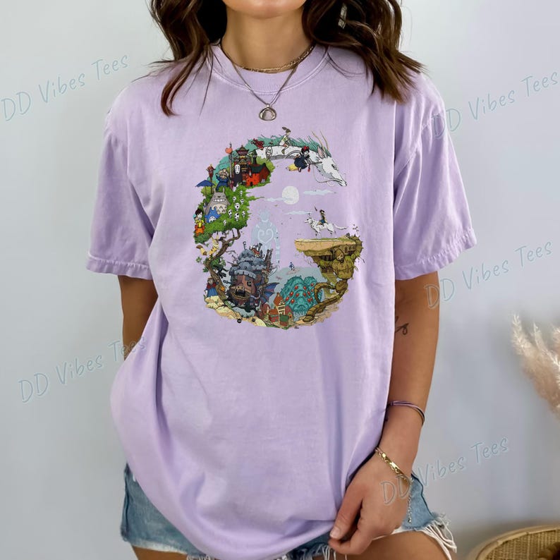 Puede incluir: Camiseta lila con un dise&ntilde;o gr&aacute;fico colorido. El dise&ntilde;o incluye un drag&oacute;n blanco, un castillo y varios personajes animados. El texto "DD Vibes Tees" est&aacute; impreso en la camiseta.