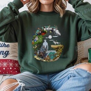 Puede incluir: Sudadera verde oscuro con un dise&ntilde;o gr&aacute;fico colorido. El dise&ntilde;o incluye ilustraciones de personajes y escenas de una pel&iacute;cula de animaci&oacute;n. La sudadera tiene mangas largas y cuello redondo. El texto "DD Vibes Tees" es visible en la imagen.