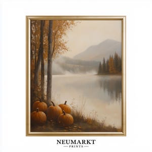 May include: A framed wall art print featuring a landscape painting of orange pumpkins resting on a grassy bank beside a calm lake. The scene includes tall trees, distant mountains, and a soft morning mist. The text NEUMARKT PRINTS appears below.