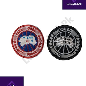 Może przedstawiać: Dwie okrągłe, haftowane naszywki. Jedna jest czerwona, biała i niebieska z napisem "Cana Goos Arct Progr". Druga jest czarna i srebrna z napisem "Nada Go Stic Gram".