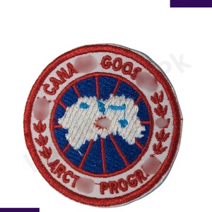 May include: Embroidered patch featuring a circular design with the text "CANA GOOS ARCT PROGR". The patch has a red border, a blue and white center with a map design, and white text. The patch is likely for clothing or accessories.