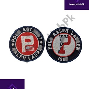 Könnte beinhalten: Zwei runde, gestickte Aufnäher mit dem Text "POLO RALPH LAUREN" an den Rändern. Ein Aufnäher hat einen roten Hintergrund mit einem weißen "P" und der amerikanischen Flagge. Der andere hat einen weißen Hintergrund mit einem roten "P" und Sternen.
