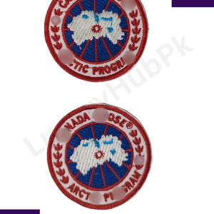 Op de afbeelding: Twee ronde geborduurde patches met een rode rand en witte tekst. De patches hebben een blauw-wit ontwerp in het midden, met de woorden "CANA GOOS ARCTIC PROGRI" en "NADA OSE ARCT PI GRAM" langs de randen.