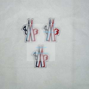 May include: Three embroidered patches featuring a stylized logo with red, white, and blue accents. The patches are on a white, textured background. The logo includes the letters "M" and a stylized design.