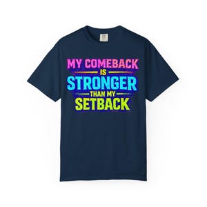 Könnte beinhalten: Marineblaues T-Shirt mit dem Text "MY COMEBACK IS STRONGER THAN MY SETBACK" in Pink, Blau, Gelb und Grün. Der Schriftzug befindet sich mittig auf der Vorderseite des Shirts. Klassischer Rundhalsausschnitt.