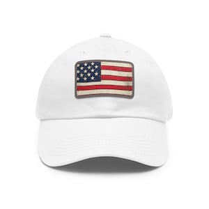Op de afbeelding: Witte baseballpet met een distressed Amerikaanse vlag patch. De patch toont de sterren en strepen in rood, wit en blauw. De pet heeft een gebogen klep en een klassiek, verstelbaar ontwerp.
