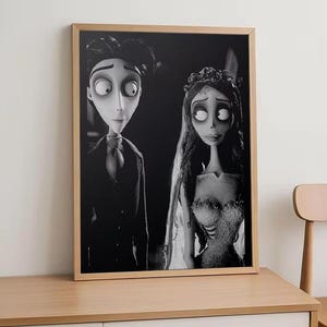 May include: Black and white framed print featuring characters from the animated film, Corpse Bride. The image shows a man in a suit and a woman in a wedding dress. The print is displayed on a wooden cabinet.