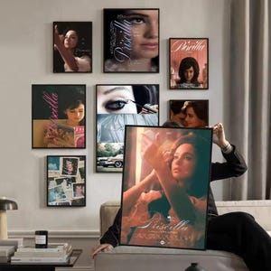 Pode incluir: Uma coleção de cartazes de filmes emoldurados do filme "Priscilla" exibidos em uma parede. Os cartazes mostram imagens da atriz, com o título do filme em uma escrita elegante. O arranjo inclui vários tamanhos e estilos, criando uma estética de galeria.