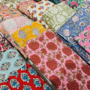 Puede incluir: Una colección de muestras de tela plegadas con varios patrones florales y botánicos estampados en bloque en colores vibrantes que incluyen rosa, rojo, amarillo, azul, verde y blanco. Cada pieza muestra motivos y diseños repetitivos distintos.