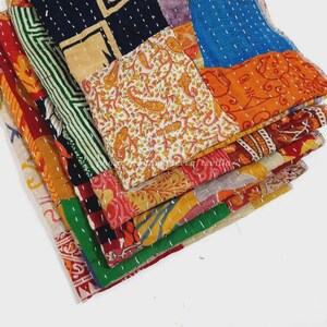 May include: A folded patchwork quilt featuring various fabric panels in vibrant colors including orange, blue, green, red, and cream. The textile displays intricate patterns such as paisley and geometric shapes, all held together by visible white running stitch embroidery.