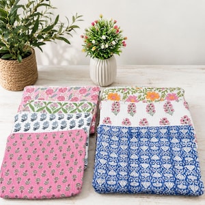 Op de afbeelding: Een collectie rechthoekige stoffen tasjes met diverse blokgedrukte bloemmotieven in tinten roze, blauw, groen en oranje. De tasjes zijn gerangschikt in twee stapels en tonen doorgestikte texturen en gedetailleerde botanische ontwerpen.