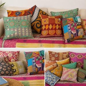 May include: A collection of square and rectangular throw pillows featuring various patchwork designs, intricate embroidery, and vibrant multi-coloured patterns including floral, geometric, and paisley motifs, arranged on a sofa with a pink and yellow throw.