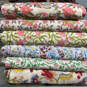 Pode incluir: Uma pilha de seis rolos de tecido dobrados com vários padrões florais. Os têxteis exibem fundos brancos com desenhos impressos em tons de rosa, verde, azul, amarelo e vermelho, apresentando motivos botânicos como flores, folhas e vinhas.