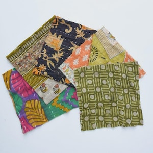 May include: A collection of six square fabric patches featuring various patterns including floral, geometric, and abstract designs in colours such as olive green, black, orange, yellow, pink, and purple, all finished with visible white running stitch quilting.