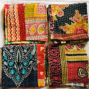 Peut inclure: Quatre piles de carrés de tissu présentant des motifs et des couleurs variés, notamment jaune, rouge, noir et bleu sarcelle. Chaque pièce est confectionnée avec des points de piqûre blancs visibles sur toute la surface du textile.