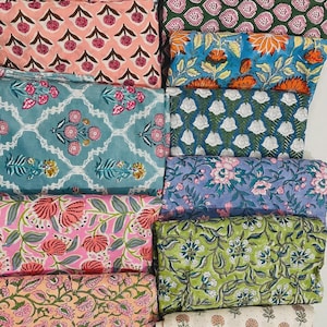 Puede incluir: Una colección de piezas de tela plegadas con diversos patrones florales estampados en bloque en colores variados, incluyendo rosa, verde, azul, naranja y blanco. Los textiles muestran motivos botánicos repetitivos, enredaderas y flores dispuestos en distintos diseños geométricos y orgánicos a lo largo de las diferentes muestras.