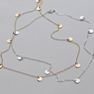 May include: A silver and gold necklace with small round charms hanging from it. The necklace is layered and has a delicate chain.