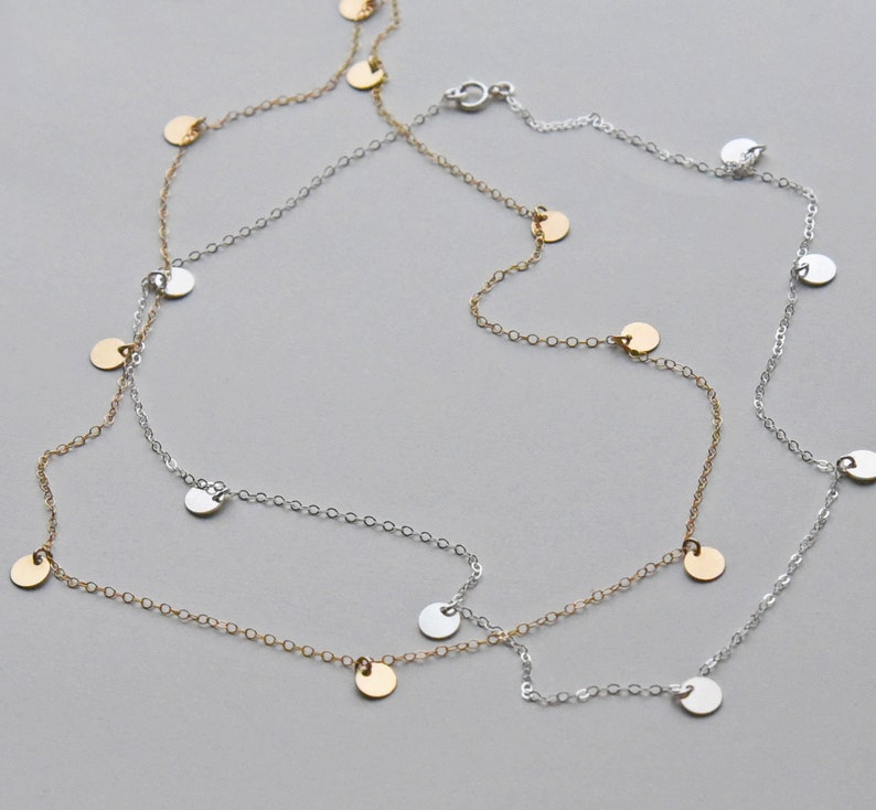 May include: A silver and gold necklace with small round charms hanging from it. The necklace is layered and has a delicate chain.