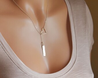 Puede incluir: Un collar de plata con un delicado dije de corazón abierto y un dije largo y delgado. El dije es texturizado y tiene un acabado martillado.