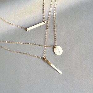 Puede incluir: Tres collares de oro con diferentes colgantes. Un collar tiene un peque&ntilde;o colgante redondo con la letra "J" grabada en &eacute;l. Los otros dos collares tienen colgantes de barra rectangular delgada.