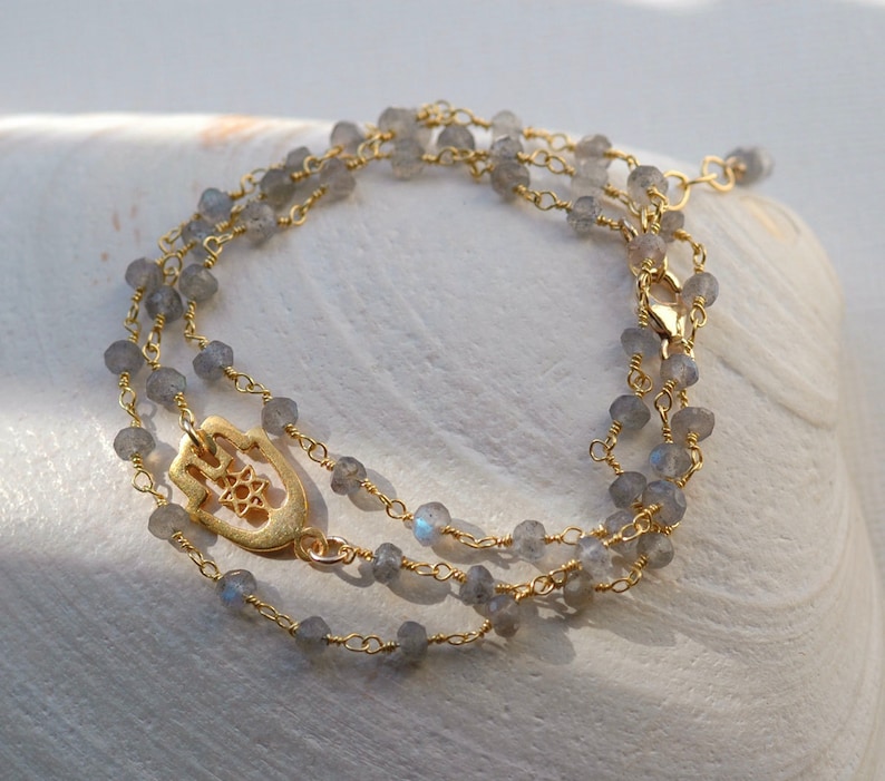 May include: A gold chain necklace with a hamsa hand charm and grey labradorite beads.