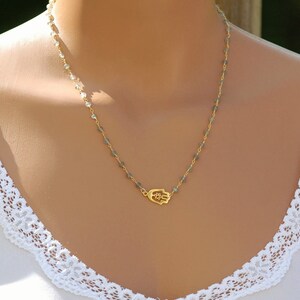 May include: A gold hamsa hand charm necklace with a delicate chain and grey beads.