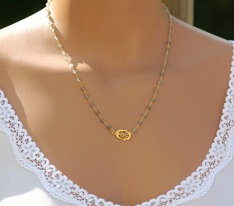May include: A gold hamsa hand charm necklace with a delicate chain and grey beads.